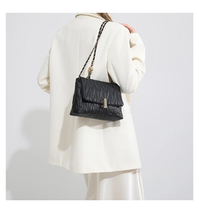 Detail of black quilted PU leather crossbody bag with elegant gold hardware and chain