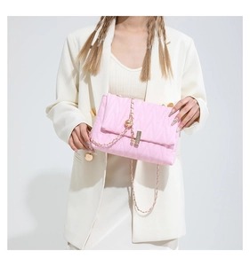 Detail of pink quilted PU leather crossbody bag with gold chain and ball charm on white suit