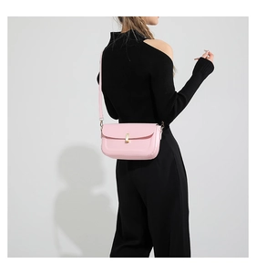 Pink PU leather crossbody bag with gold buckle shown on black knitwear