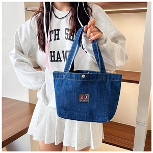 Détail du sac cabas en denim avec écusson carré brodé du numéro 23 rouge et logo discret