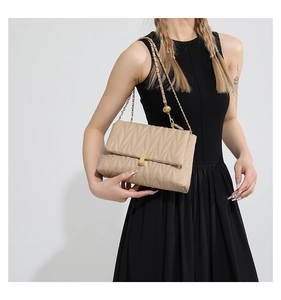 Detail of apricot wavy quilted crossbody bag with golden clasp and chain strap