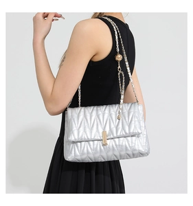 Detail of silver quilted PU leather bag featuring gold lock and chain strap on a model
