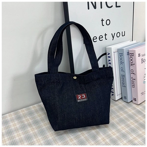 Gros plan détaillé d'un sac cabas en denim bleu avec écusson rouge et bouton pression