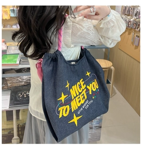 Dettaglio della borsa tote in denim blu scuro con scritte gialle e manici rosa