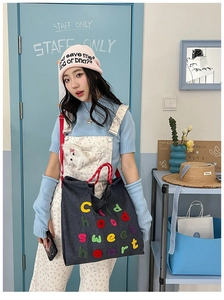 Dettaglio di una borsa tote in denim grigio scuro con testo ricamato in 3D colorato