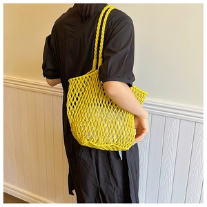 Detail of a bright yellow woven mesh tote bag held by a model in casual attire