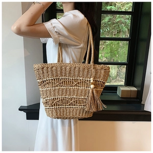 Détail d'un sac cabas en paille avec texture tressée et pompon sur robe blanche