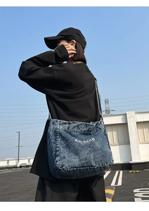 Macro shot of blue denim crossbody bag with white embroidery on a casual outdoor model