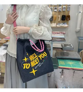 Dettaglio della borsa tote in denim blu con ricami gialli e tracolla rosa
