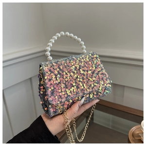 Detail of glitter party clutch with pearl handle and golden chain strap in hand