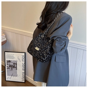 Detail of a chic black sequin shoulder bag with silver chain strap worn by a model