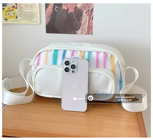 Close-up of white nylon crossbody bag with colorful stripes next to a phone for size
