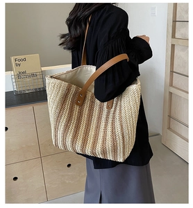 Detail view of large straw tote bag featuring brown leather straps and woven texture