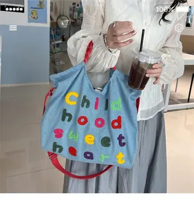 Borsa tote in denim azzurro con ricamo colorato e tracolla rossa indossata da modella
