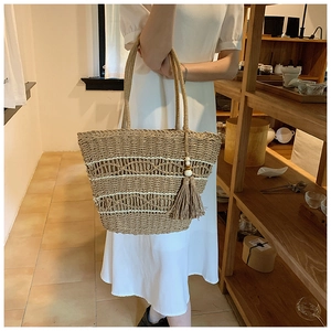 Détail d'un grand sac cabas en paille tissée avec motifs ondulés et pompon à franges chic
