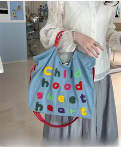 Dettaglio della borsa tote in denim azzurro con ricami colorati e manici intrecciati rossi