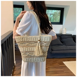 Sac fourre-tout en paille tissée avec pompons et rayures porté par un modèle