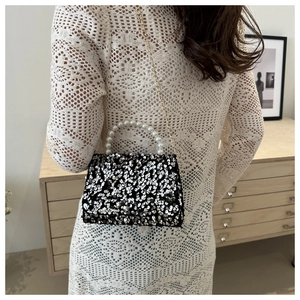 Detail of black sequin handbag with pearl handle and golden chain on a white dress model