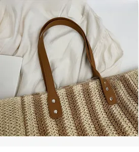 Detail of woven straw tote bag with brown leather handles and silver rivet hardware
