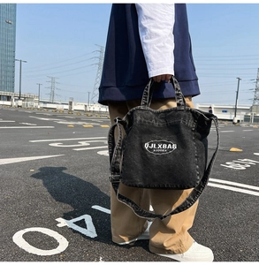 Detailed street shot of a black washed denim tote bag with logo and adjustable strap