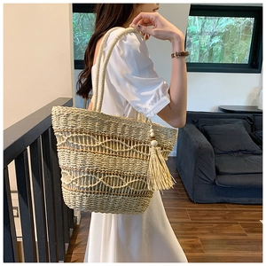 Détail du sac cabas en paille tissée avec coutures contrastées et pompon en bois