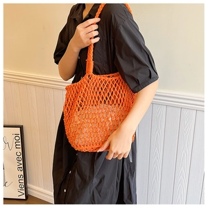 Close-up of a vibrant orange hand-woven mesh tote bag carried by a model over the shoulder