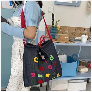 Dettaglio borsa a tracolla in denim blu con ricamo a spugna e tracolla in tessuto rosso