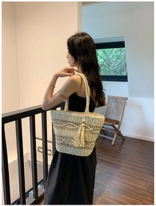 Détail d'un sac cabas en paille beige avec crochet ondulé et breloque à pompon élégante