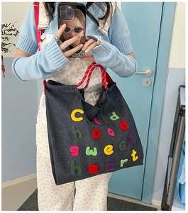 Dettaglio della borsa tote in denim scuro con ricamo colorato e manici in corda rossa