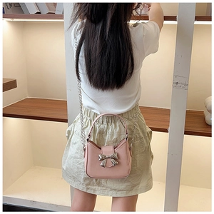 Pink PU leather handbag with silver bow detail and chain strap worn by a model