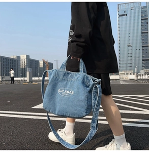 Outdoor shot of a washed denim tote bag with white logo and adjustable strap