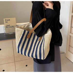 Detail of blue and white striped straw tote bag featuring brown leather shoulder straps