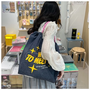 Dettaglio della borsa tote in denim con ricamo giallo e tracolla a quadretti su modella
