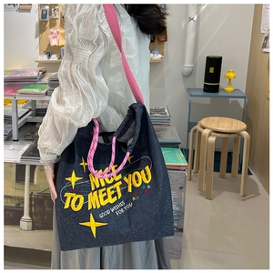 Dettaglio della borsa tote in denim blu con cinghie rosa e ricamo giallo in negozio