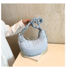 Close-up of light blue quilted crescent bag with ruffled handle and zipper detail