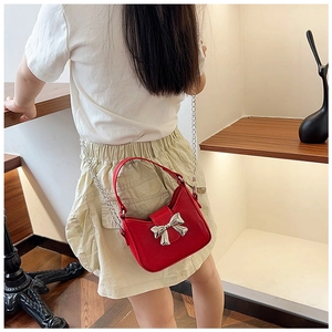 Detail of red PU leather child handbag with silver bow accent and metal chain strap