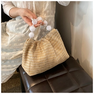 Détail de la texture du sac en paille tressée avec poignée élégante en perles blanches