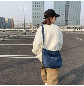 Detail of dark blue denim tote bag with white oval logo embroidery and wide strap