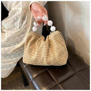 Détail du sac à bandoulière en paille avec poignée en perles blanches et texture naturelle