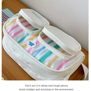 White nylon shoulder bag with soft rainbow stripes and a blue circular logo on wood surface