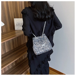 Detail view of a silver sequined bucket bag with metallic chain on a female model