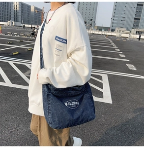 Detail of trendy blue denim crossbody bag with logo on white waffle textured sweatshirt