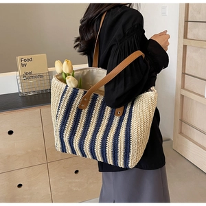 Detail of a large straw tote bag with navy blue stripes and brown leather handles