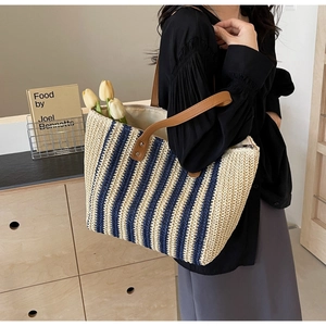 Detail view of woven straw tote bag with navy stripes and brown leather handles