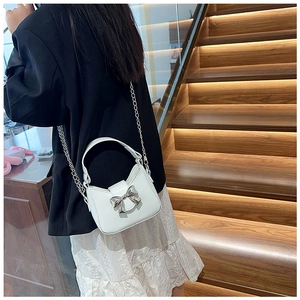 Detail of white PU crescent bag with silver metallic bow and chain strap on a model