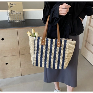Detail of straw woven tote with navy stripes, brown leather handles and metal rivets