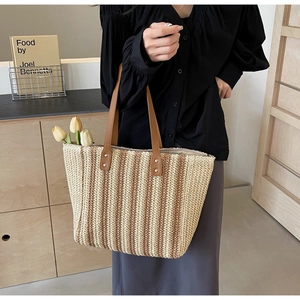 Detail of woven straw tote bag featuring brown faux leather handles and vertical stripes