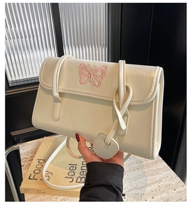 Close-up of cream PU leather shoulder bag featuring pink butterfly embroidery and heart charm