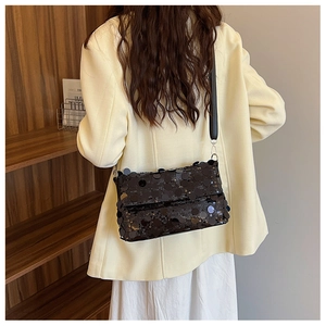 Detail of a large black sequin crossbody bag styled on a beige blazer for a modern look
