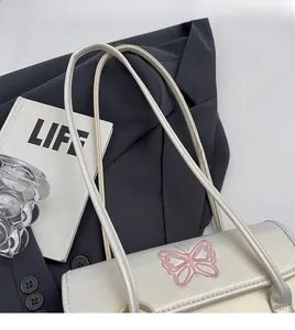 Detail of white PU shoulder bag featuring pink butterfly embroidery and sleek straps